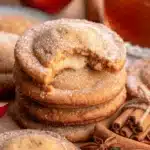 Freshly baked apple cider cheesecake cookies stacked on a table with spiced sugar.